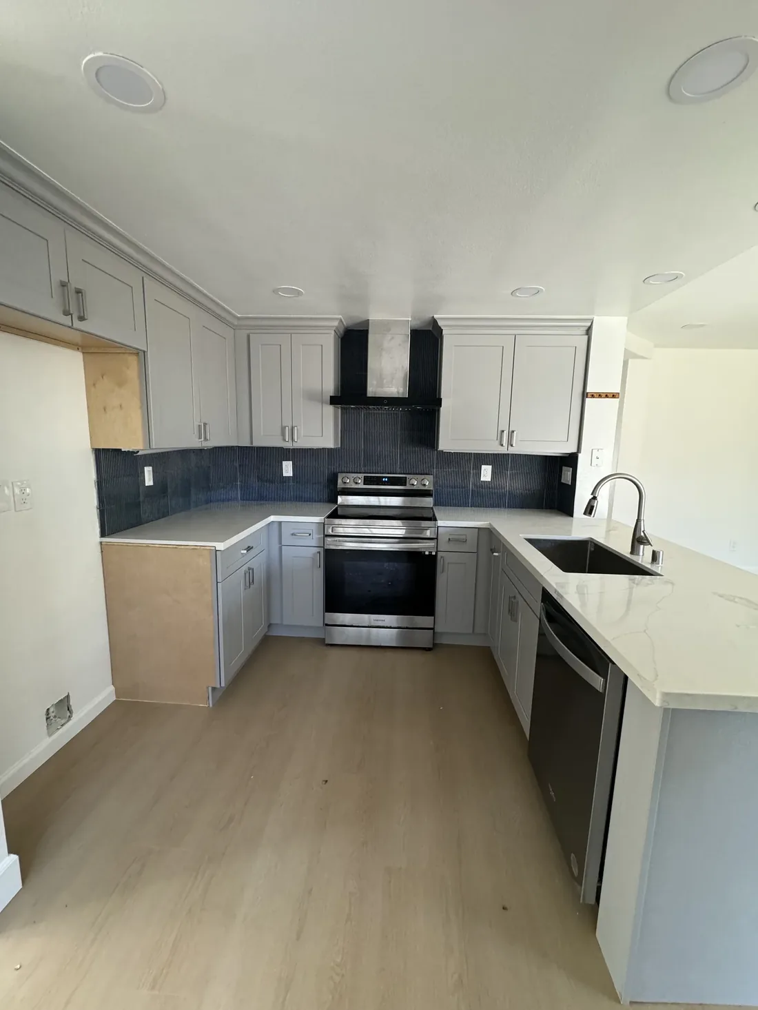 Remodeled kitchen with gray shaker cabinets, navy tile backsplash and quartz countertops