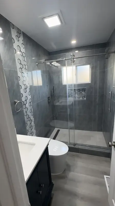 Contemporary gray-tile bathroom with glass shower and mosaic accent stripe